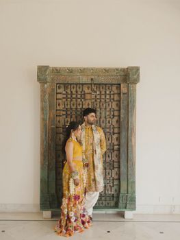 A couple dressed in vibrant traditional clothing stands elegantly by an intricately carved wooden door, capturing cultural beauty.