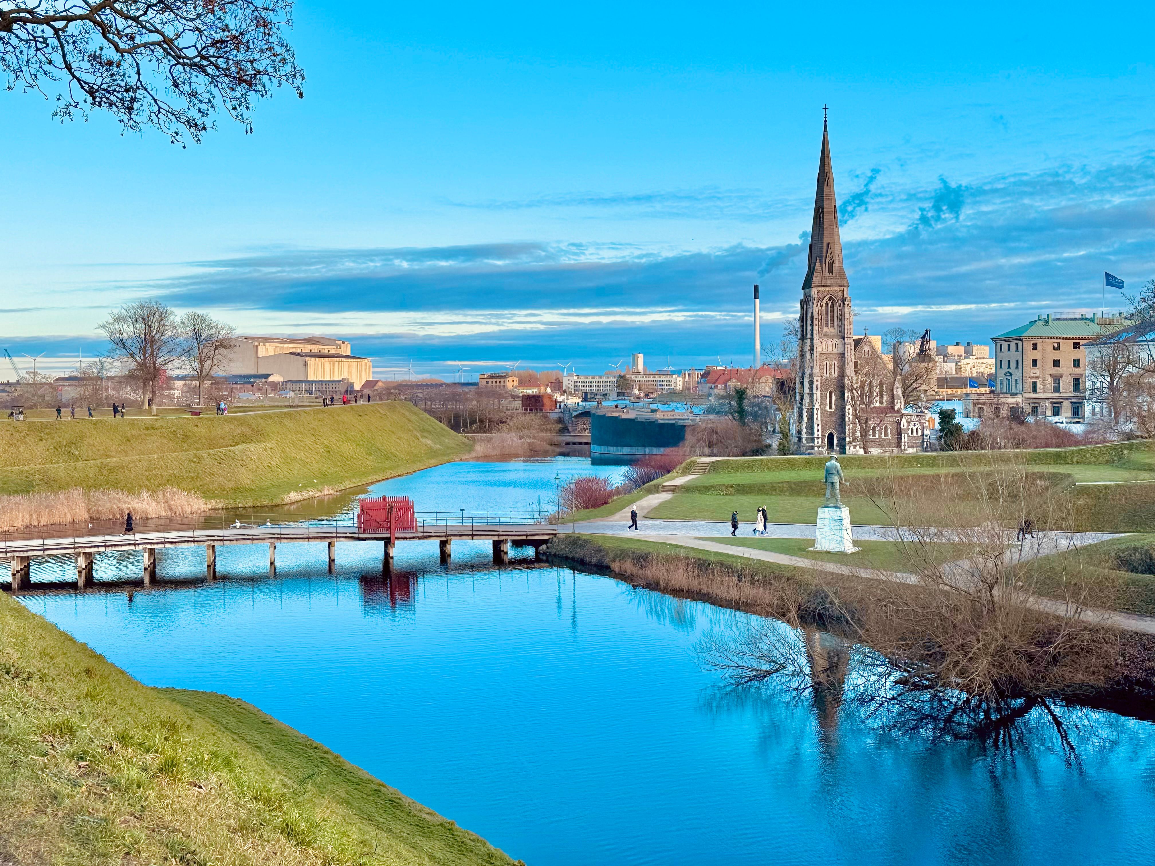 Sunny view of Copenhagen's Kastellet fortress with iconic church and lush greenery.