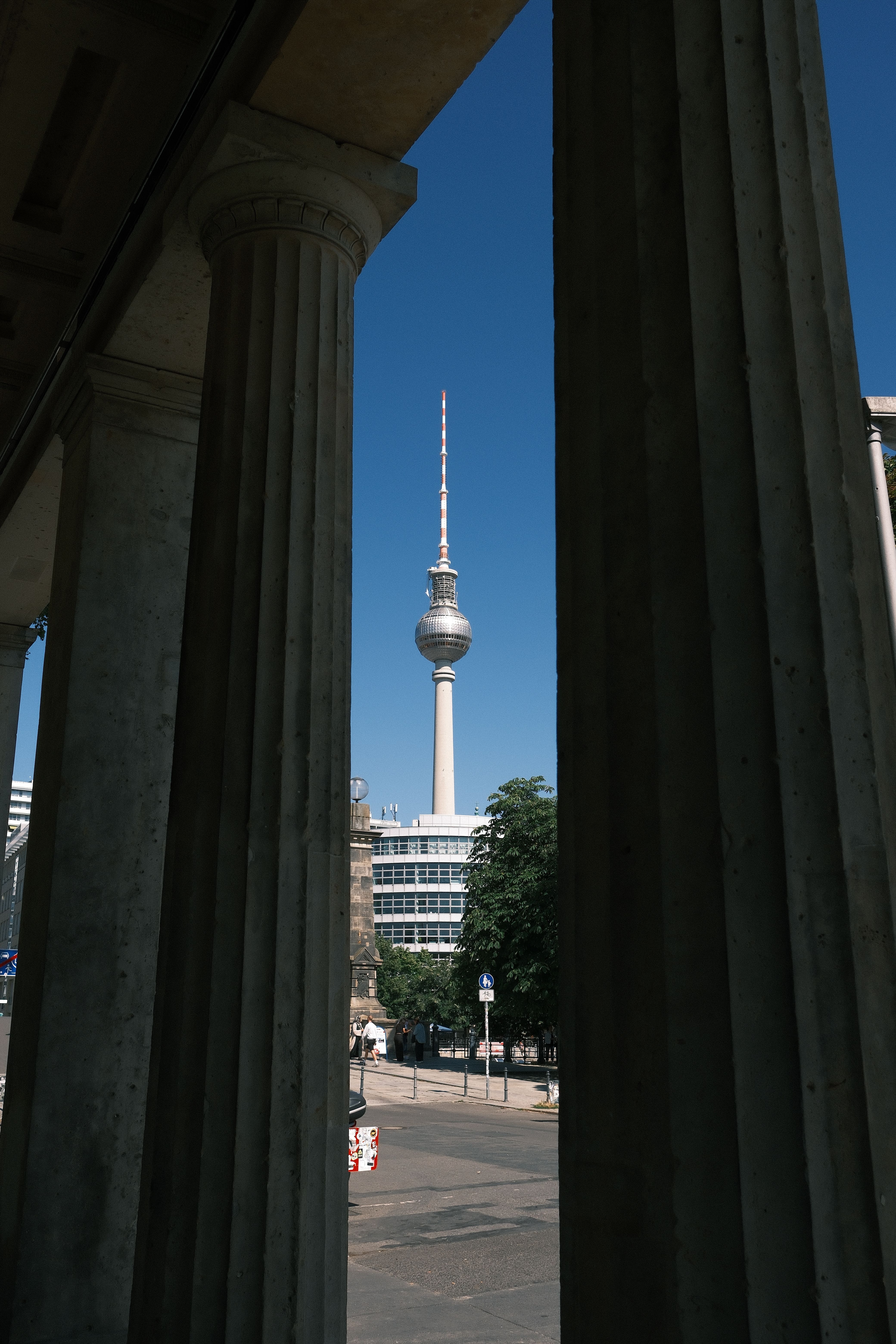 The iconic Berlin TV Tower framed by historic columns on a sunny day.