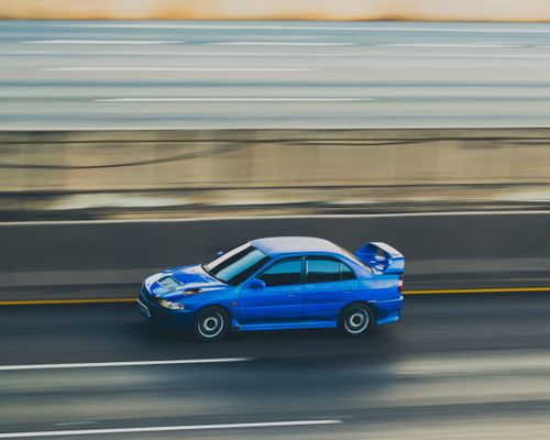 Free Dynamic shot of a blue car captured in panning motion on a highway. Stock Photo