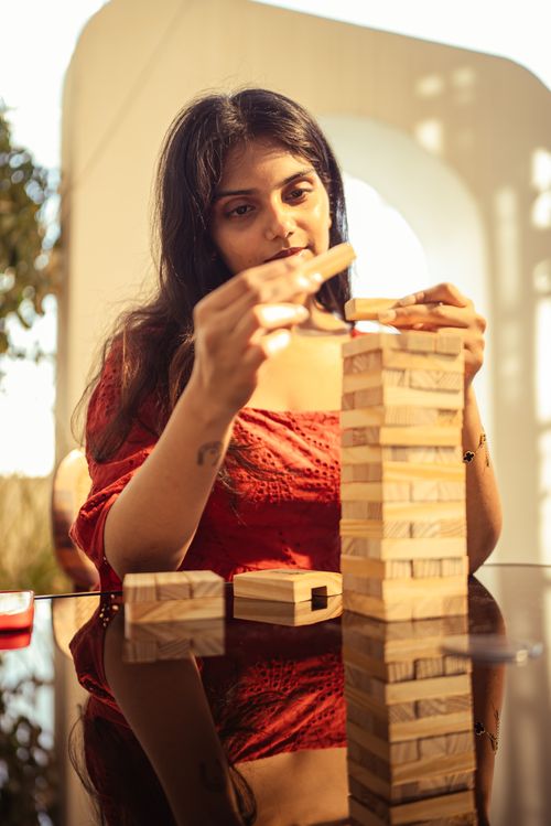 Free A woman playing Jenga in a bright outdoor setting, reflecting focus and fun. Stock Photo
