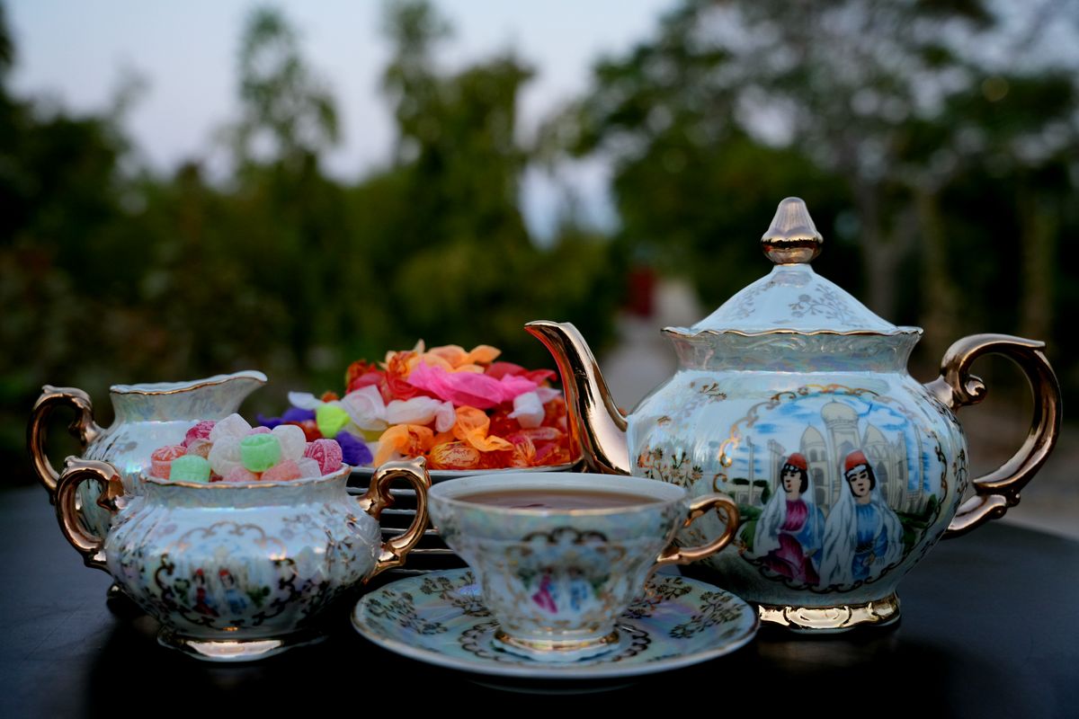 Beautiful porcelain tea set and colorful candies on a table outdoors, perfect for a summer afternoon tea.