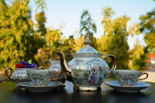 Free Beautiful ornate porcelain tea set on a table with a blurred nature background, perfect for afternoon tea themes. Stock Photo