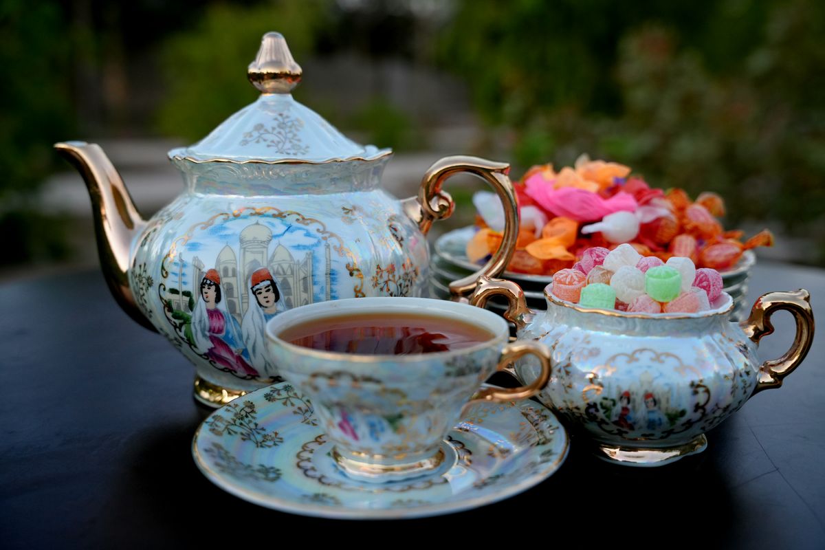 Exquisite tea set with decorative teapot, cup, and colorful candies outdoors.