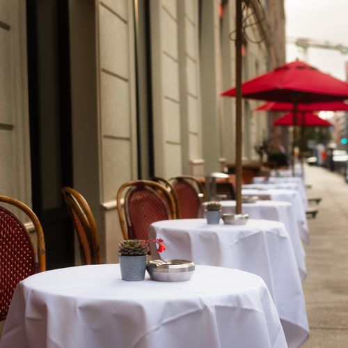 Free Elegant outdoor café tables with red umbrellas and potted plants on a city sidewalk. Stock Photo