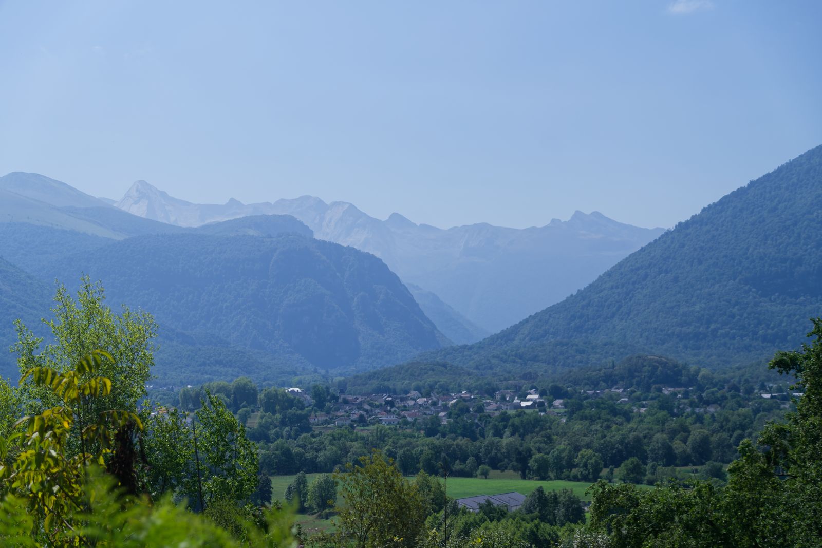 Village pyrénéen ensoleillé, niché dans une vallée et encadré de sommets rocheux lointains