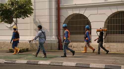 Free Group of construction workers walking along a city street under clear daylight conditions. Stock Photo