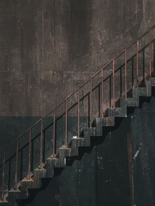 Free A rustic metal staircase ascends against a textured, dark wall, creating a striking contrast. Stock Photo
