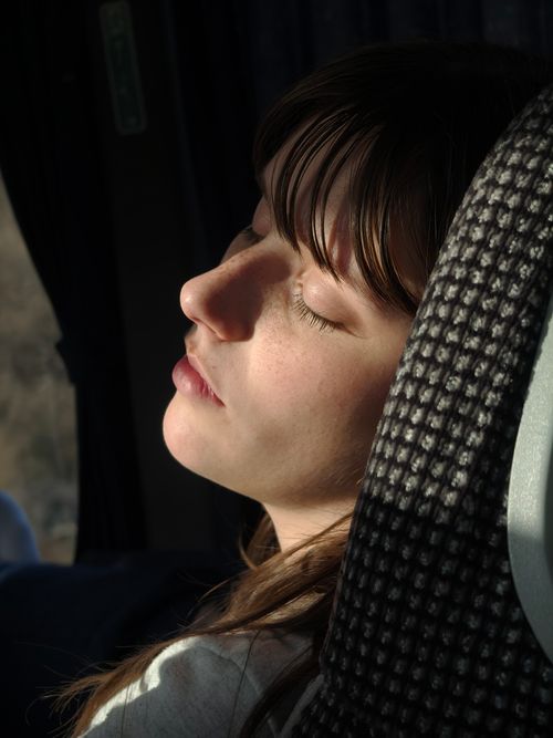 Free A young adult woman peacefully sleeping while traveling on a bus, sunlight on face. Stock Photo