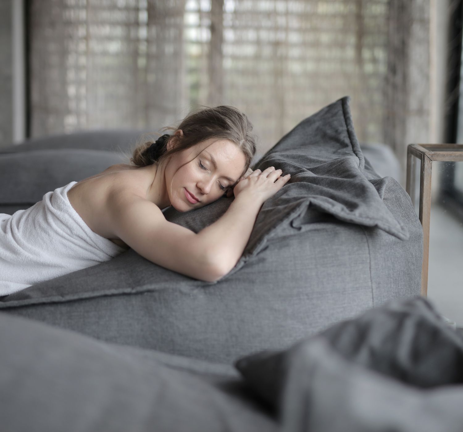 Woman peacefully relaxing at a spa, wrapped in a towel on a comfortable bed, enjoying sere
