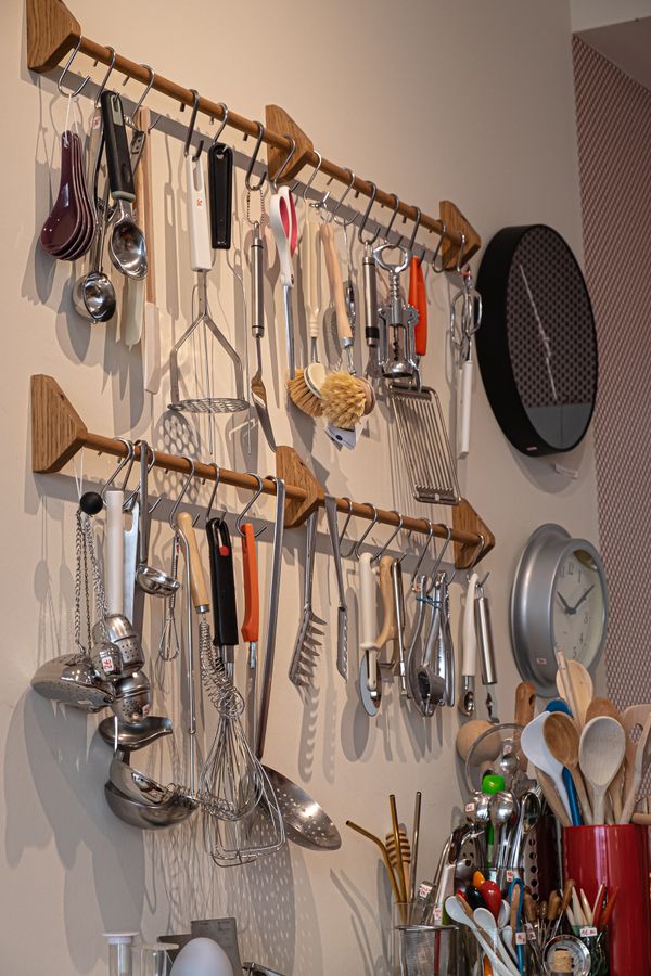 Cooking utensils hanging from hooks on a wall rail in a small kitchen