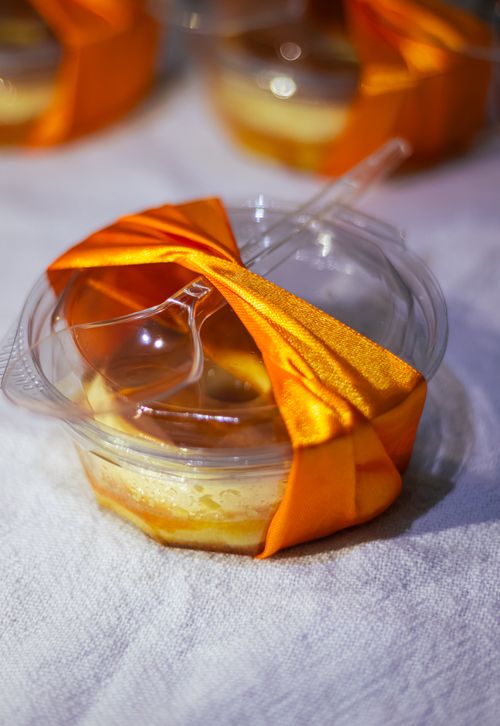 Free Elegant creme brulee dessert in a plastic cup, wrapped with an orange ribbon and spoon, on a white tablecloth. Stock Photo