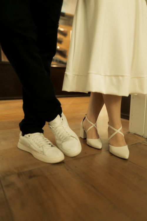 Free Close-up of a couple's feet in elegant white and black attire on a wooden floor indoors. Stock Photo