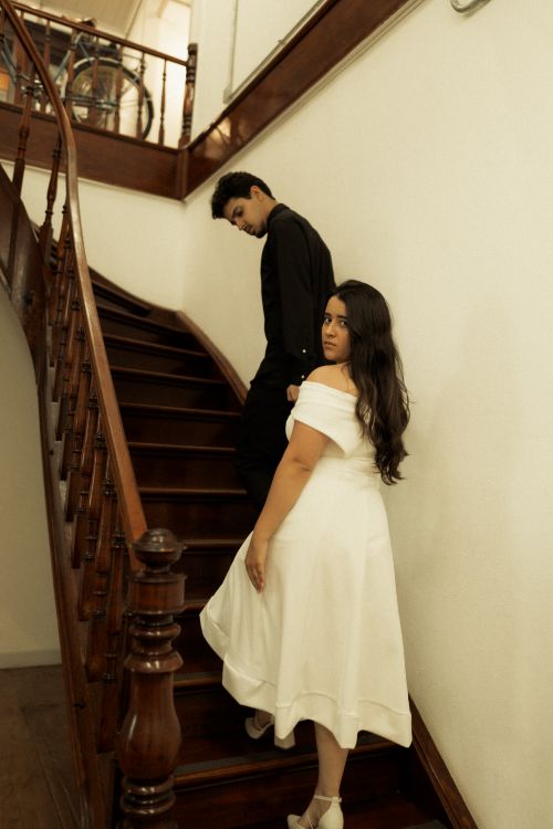 Free A couple elegantly ascends a classic wooden staircase in an indoor setting, capturing a timeless moment. Stock Photo