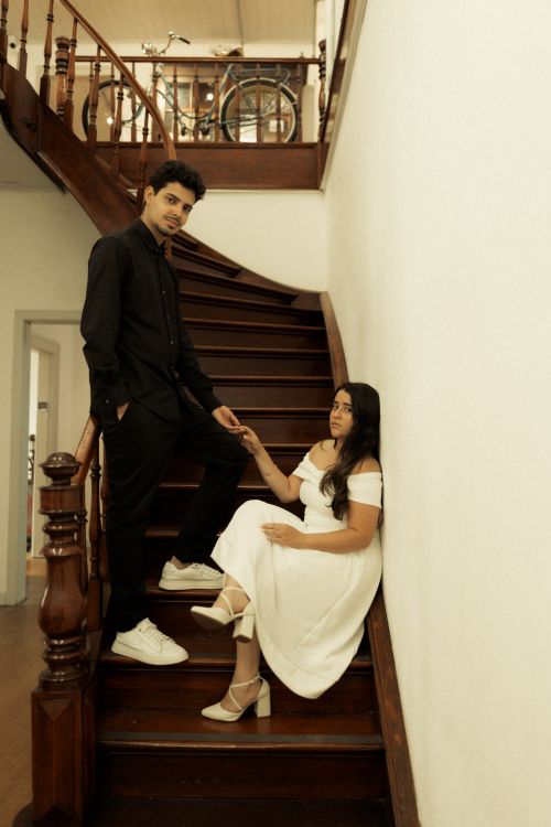 Free Stylish couple posing on a wooden staircase in a warm, vintage indoor setting. Stock Photo