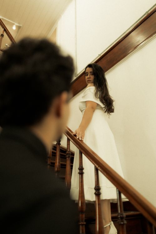 Free A woman in a white dress gracefully descends a wooden staircase indoors. Stock Photo
