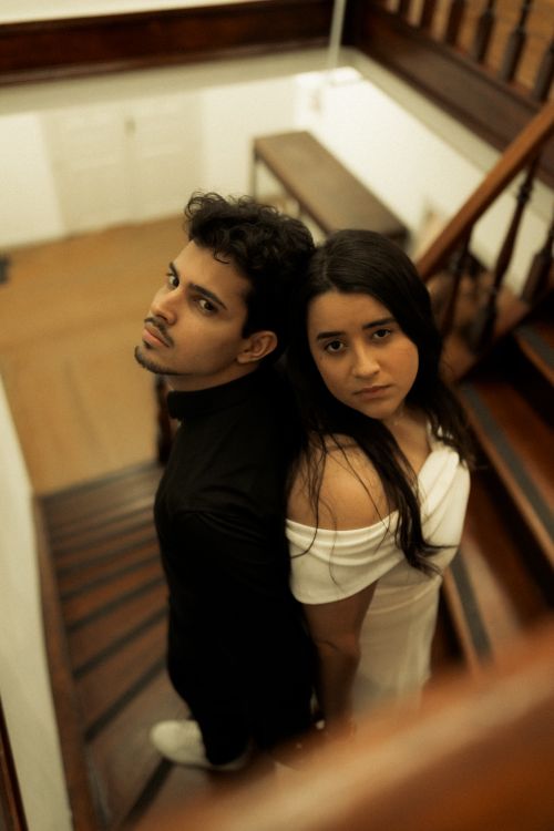 Free Elegantly dressed couple standing back to back on a classic wooden staircase indoors. Stock Photo