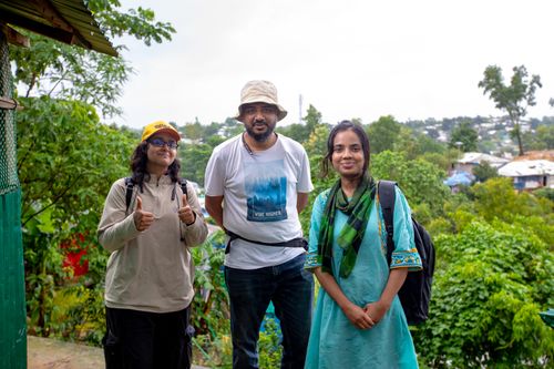 Free Three adults stand together smiling at a Bangladeshi refugee camp amidst lush greenery. Stock Photo