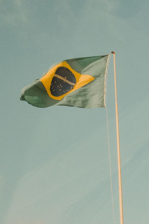Free Brazilian flag prominently waving against a clear sky, capturing patriotic spirit in Natal, RN. Stock Photo
