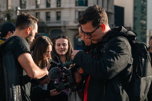 A diverse group of filmmakers collaborates outdoors, reviewing footage on a professional camera.