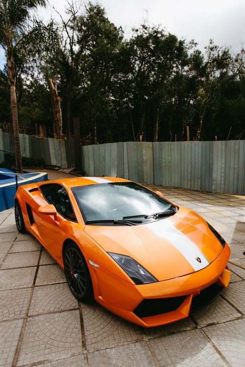Free A vivid orange Lamborghini sports car parked outside on a sunny day. Stock Photo