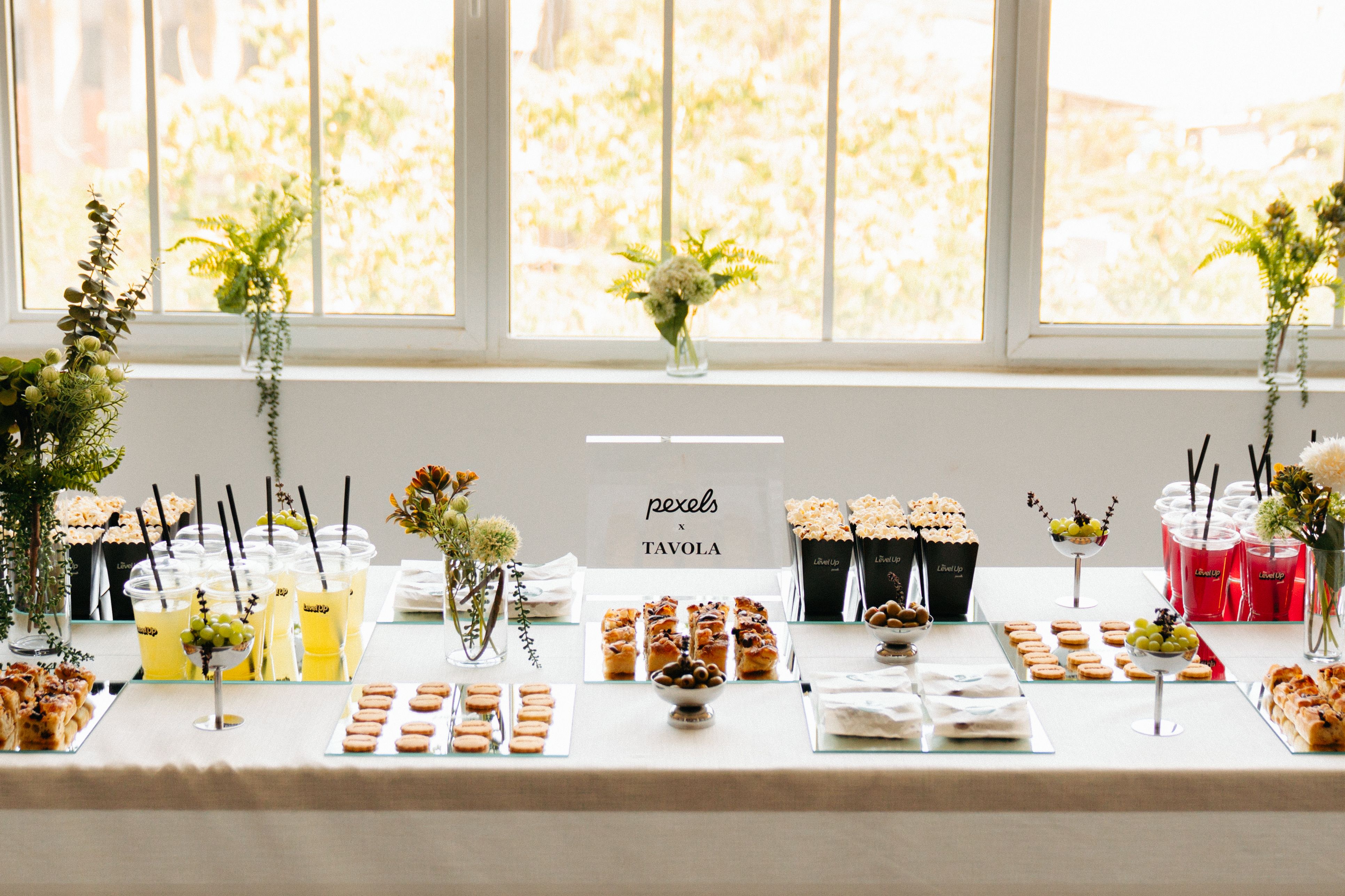 Beautifully arranged buffet table with snacks, drinks, and floral decorations at an indoor event.