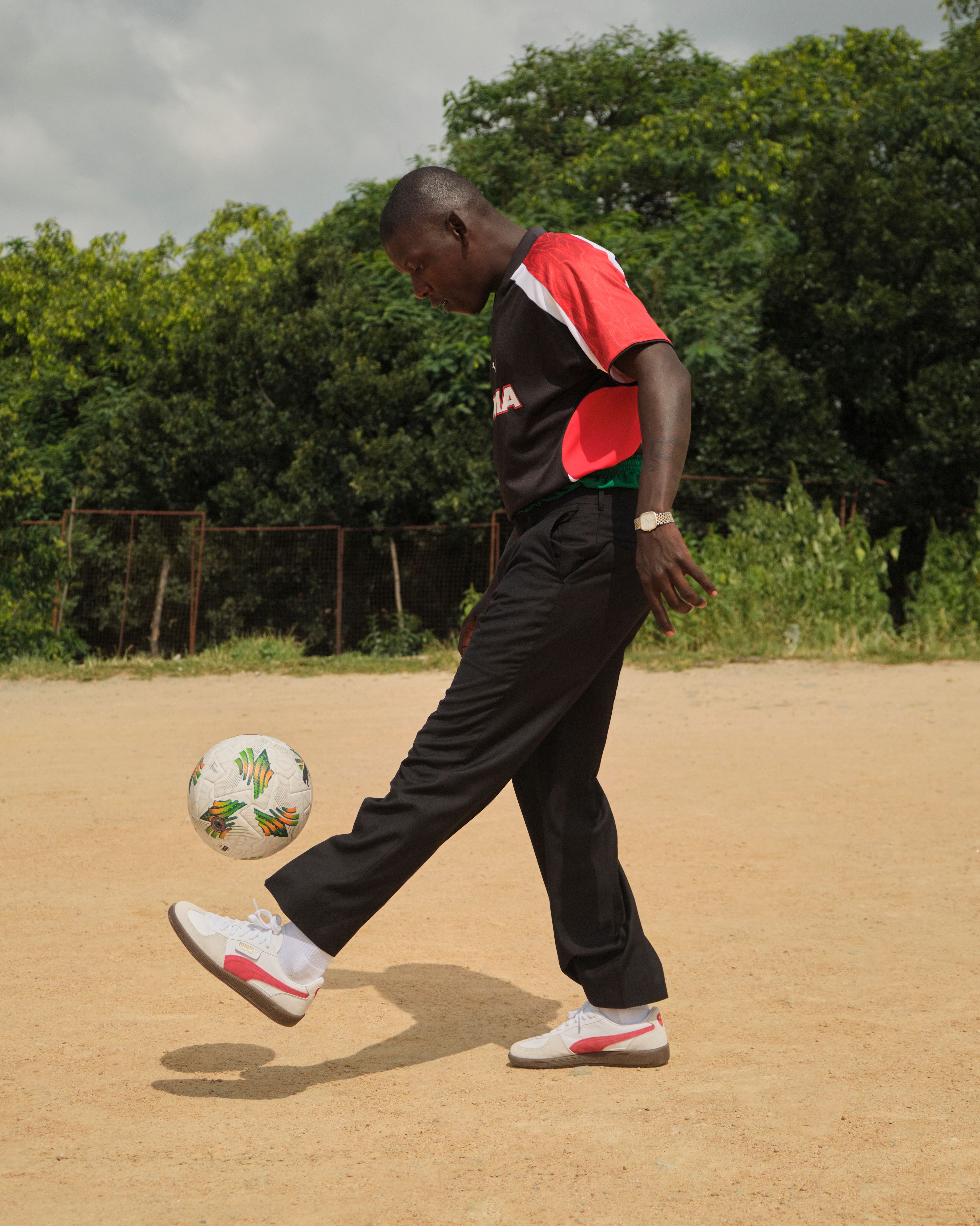 Adult man in action juggling a soccer ball outdoors on a dirt field.