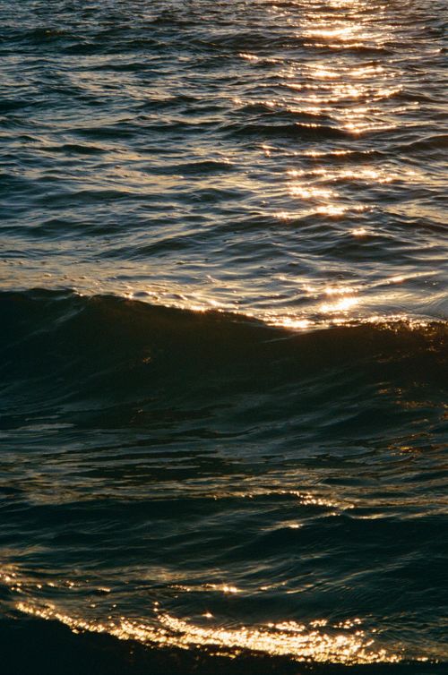 Free Close-up of shimmering sunlight reflecting on ocean waves at sunset, creating a golden hue. Stock Photo