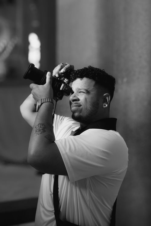 Free Black and white image of a photographer concentrating as he takes a shot indoors. Stock Photo