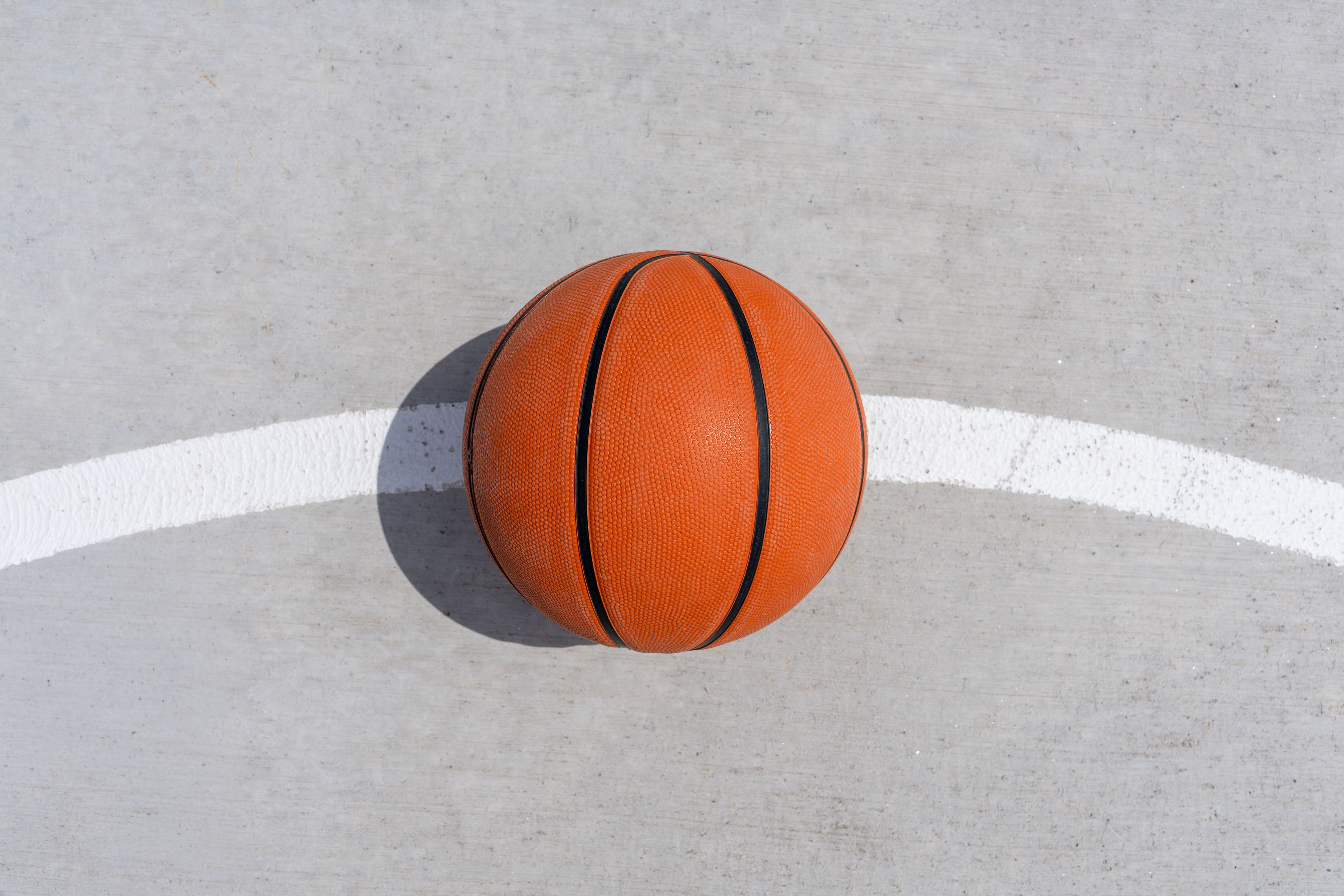A single basketball rests on the concrete of an outdoor court, capturing a minimalist sports theme.