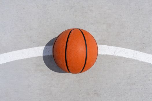 A single basketball rests on the concrete of an outdoor court, capturing a minimalist sports theme.