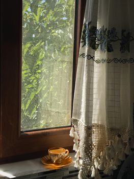 A cozy window view with sunlight streaming through a floral curtain, accompanied by a teacup.