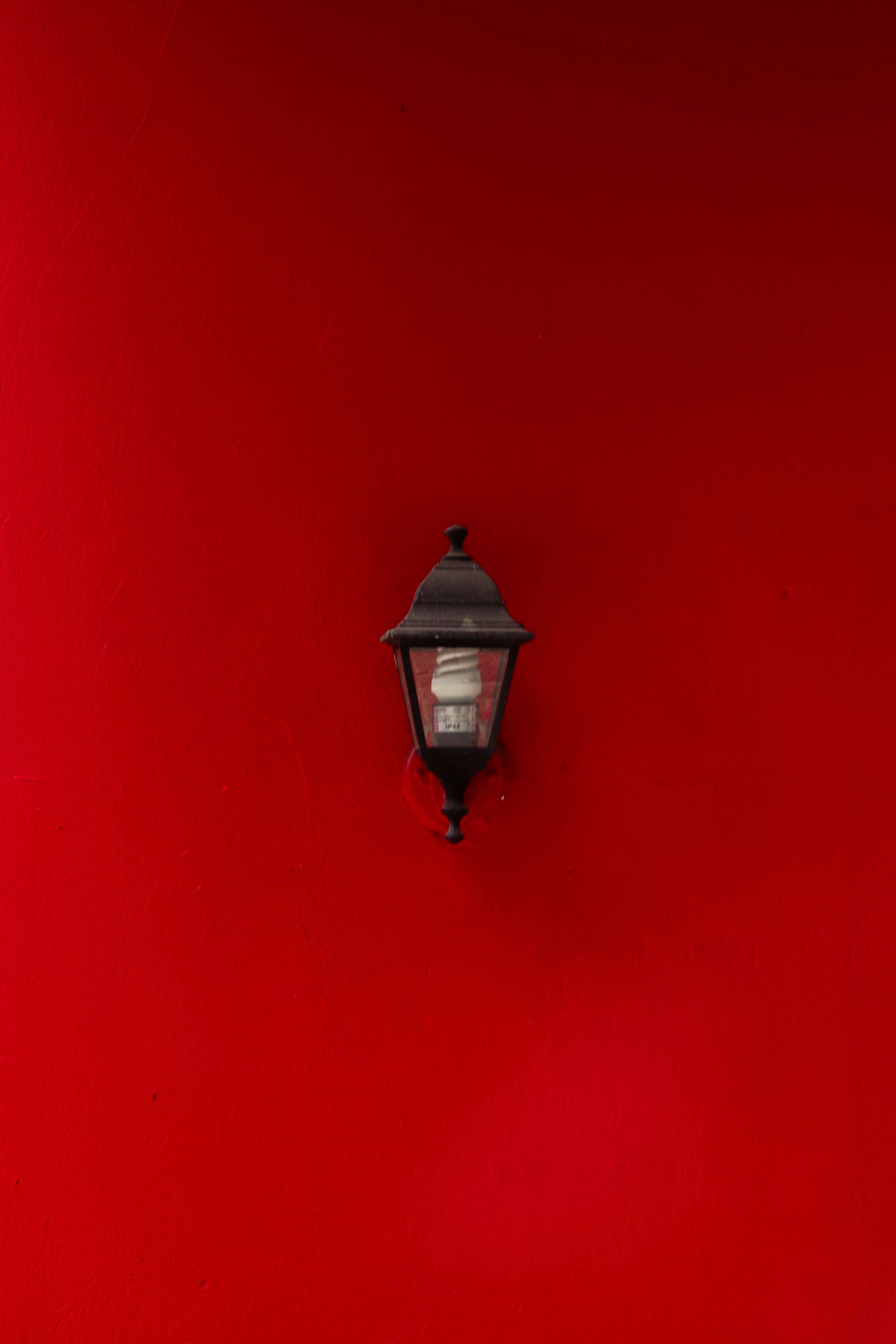 A classic black lantern set against a vivid red wall, creating a striking contrast.