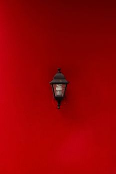 A classic black lantern set against a vivid red wall, creating a striking contrast.