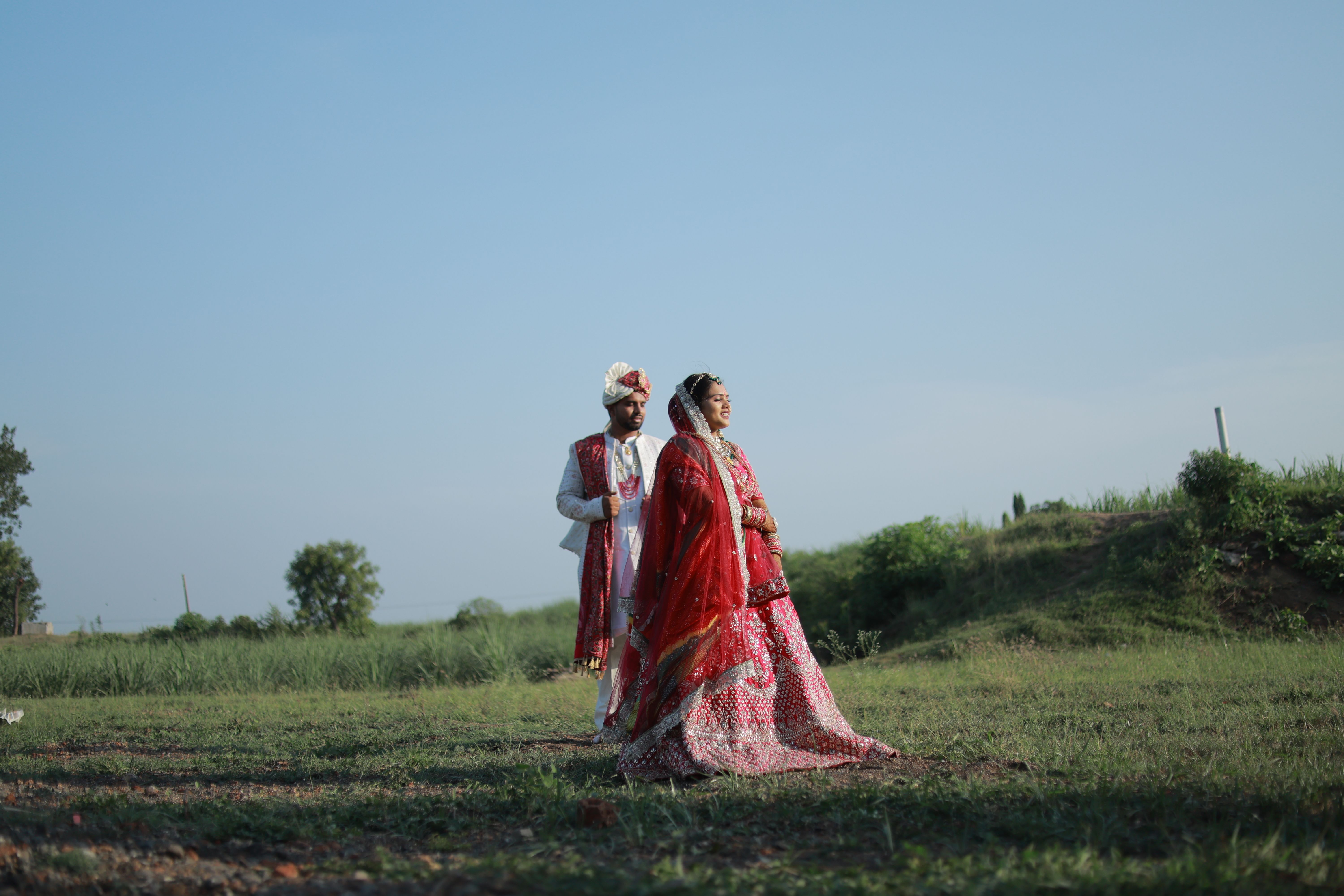 A couple in traditional Indian wedding attire posing beautifully outdoors during a sunny day.
