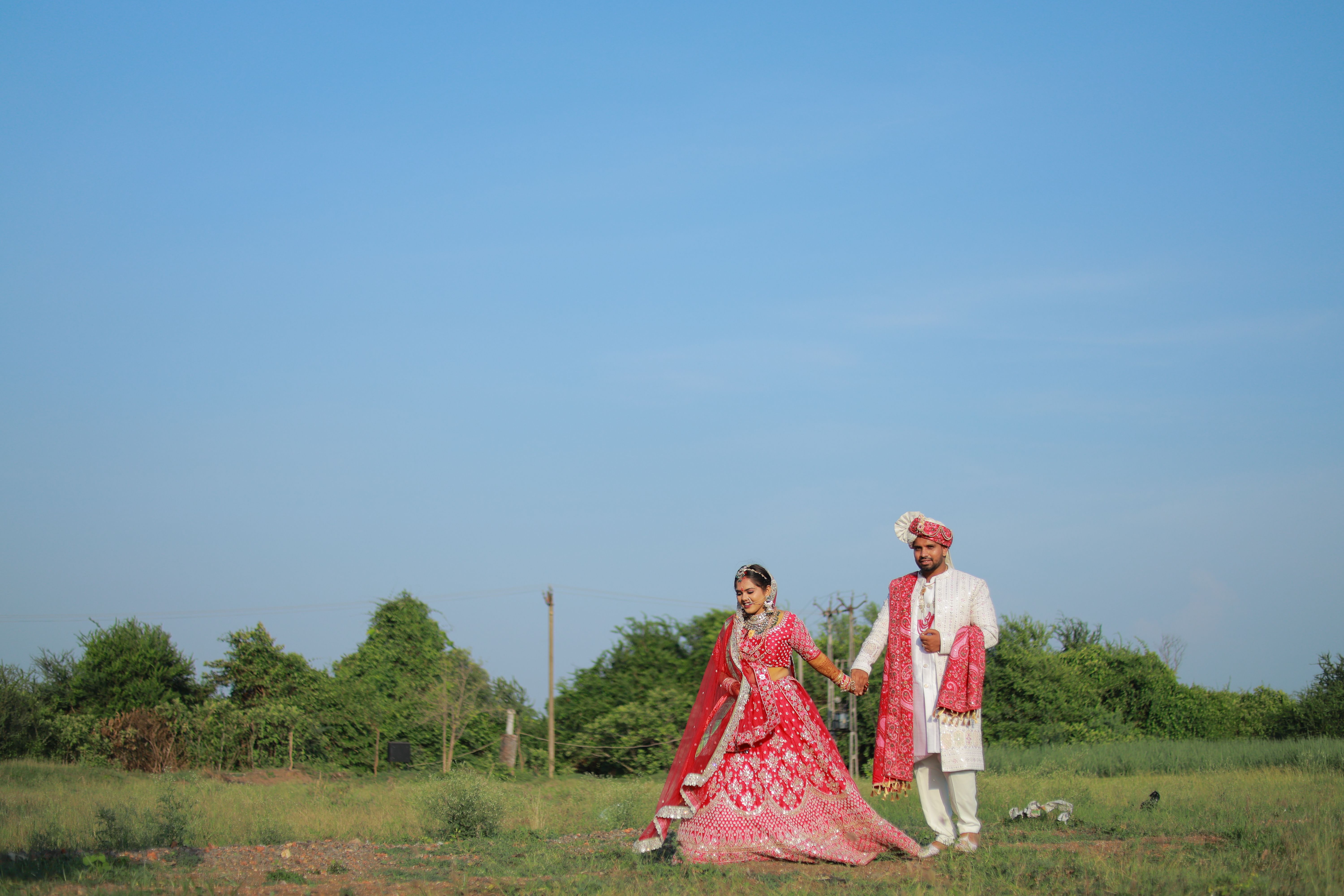 Beautiful Indian bride and groom holding hands outdoors at sunset. Traditional attire in a serene landscape.