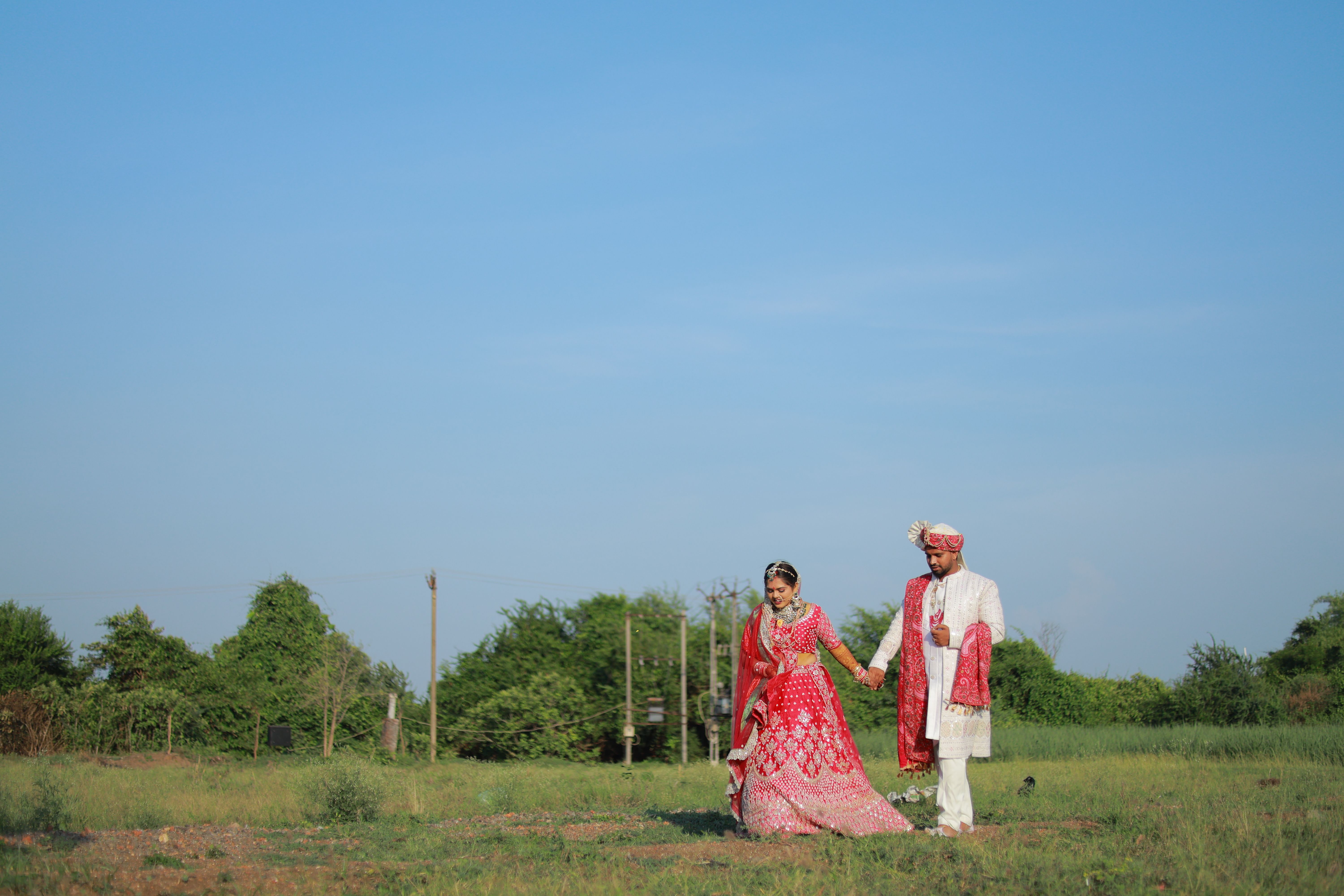 Elegant Indian bride and groom in traditional attire walking hand in hand in a scenic outdoor setting.