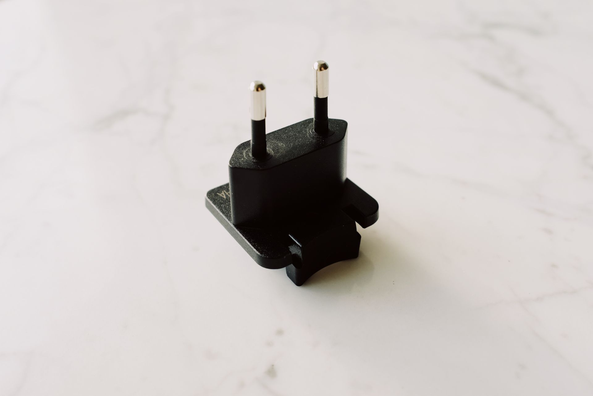 A close-up shot of a black electrical adapter on a white marble surface.