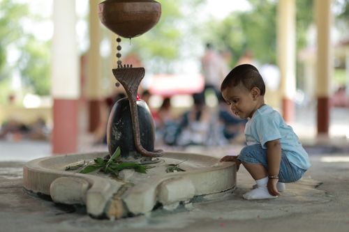 Free Adorable baby exploring a Shiva Lingam with curiosity in a spiritual setting. Stock Photo