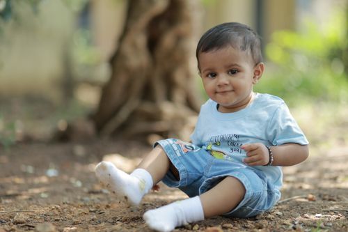 Free Cute baby sitting on the ground outdoors, wearing casual blue outfit and smiling. Stock Photo