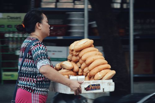 Free A woman carries a basket of fresh baguettes on a street, showcasing daily life and food culture. Stock Photo