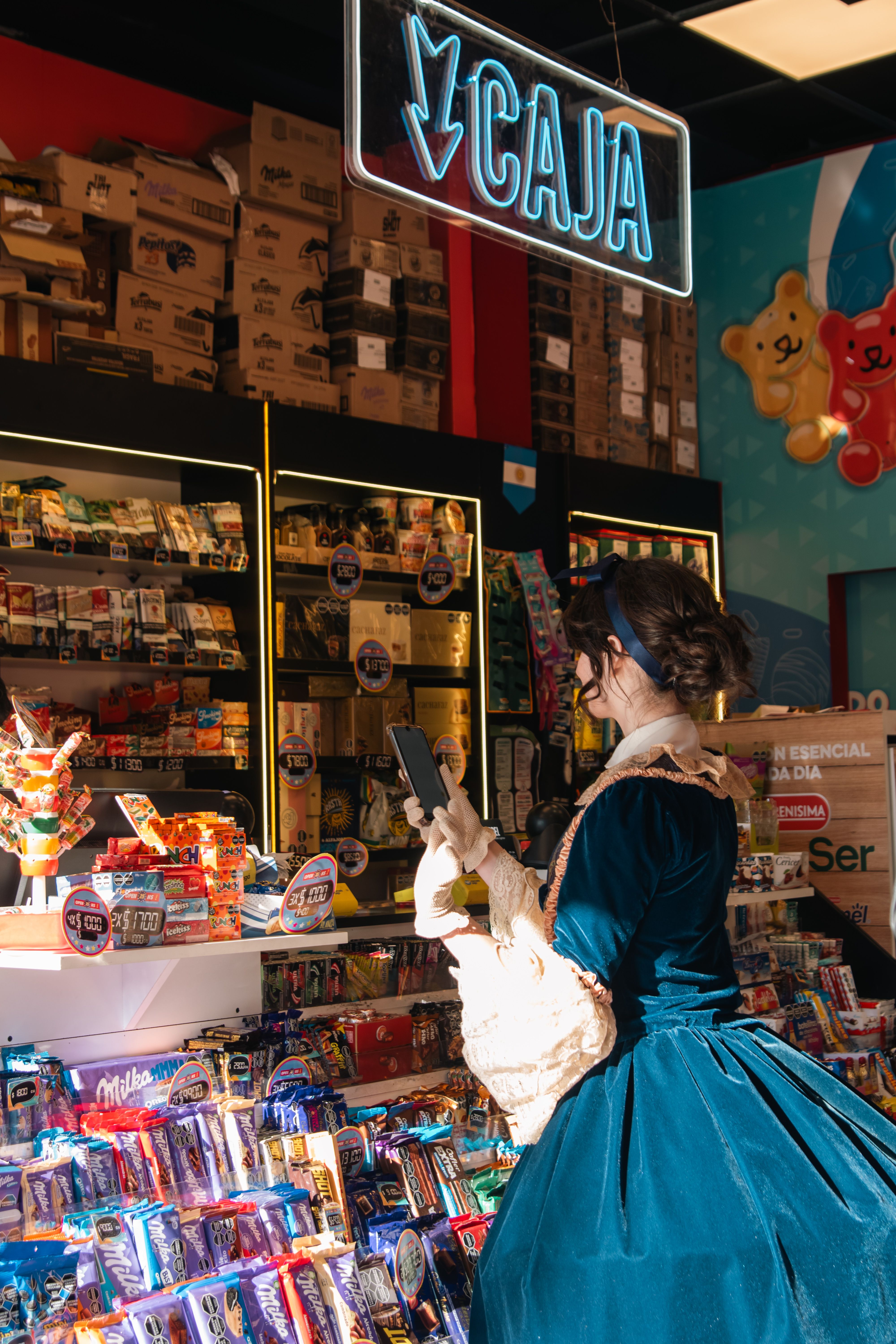 A woman in a vintage dress shops at a candy store counter under a neon 'caja' sign.