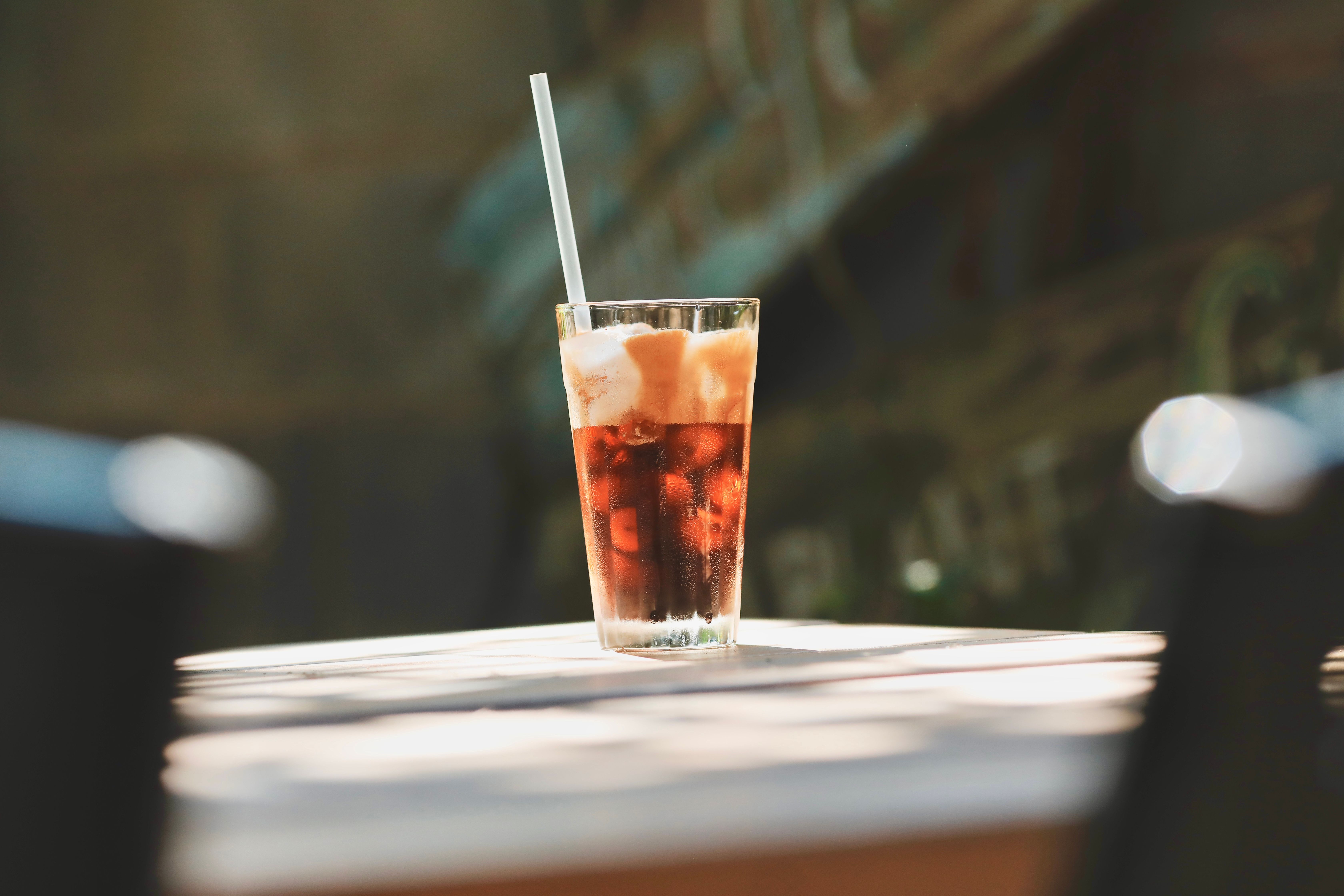 A cool glass of iced coffee with a straw on a sunlit table outdoors, perfect for summer refreshment.