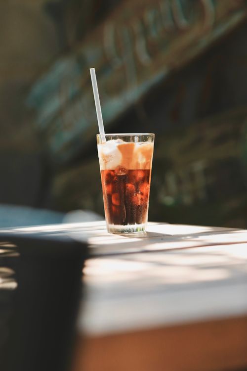 Free Tall glass of iced coffee with a straw on a sunlit table, perfect summer refreshment. Stock Photo