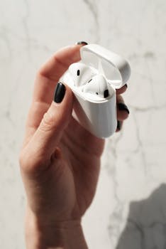 Close-up of a woman's hand holding wireless earbuds in a case against a marble background.