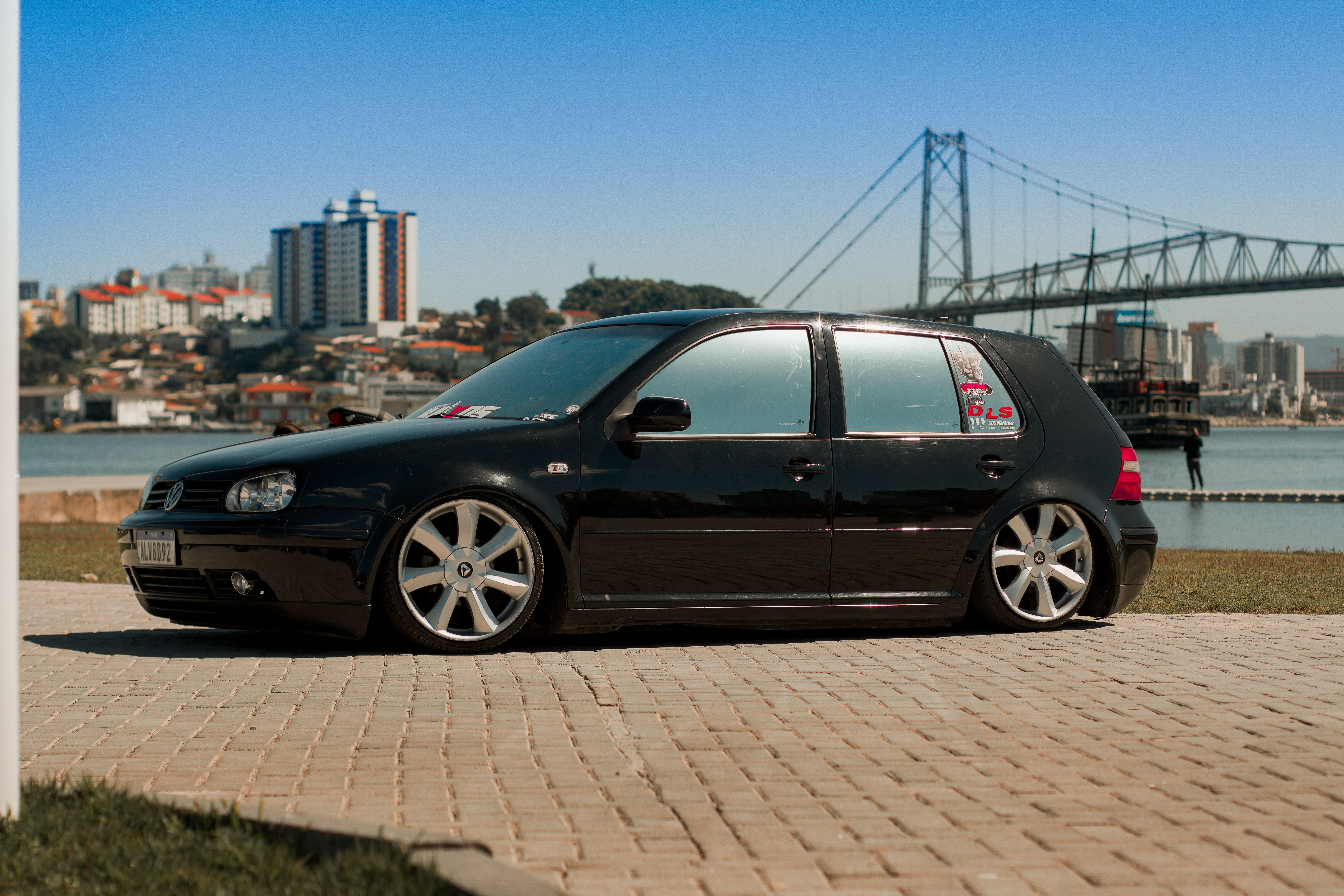 A sleek black car parked beside a famous suspension bridge in a cityscape setting.