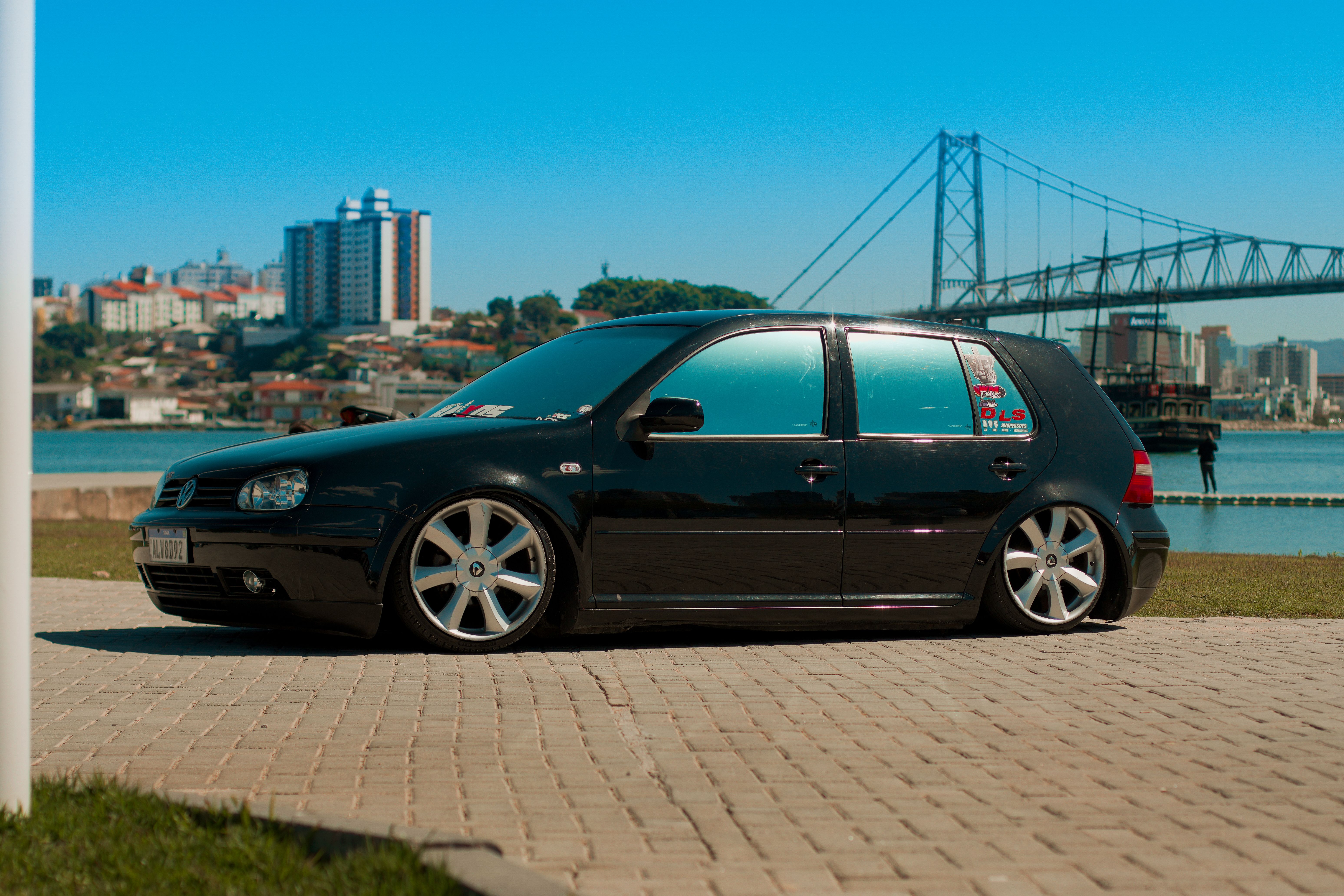 Sleek black car parked by scenic Florianópolis bridge in daylight.