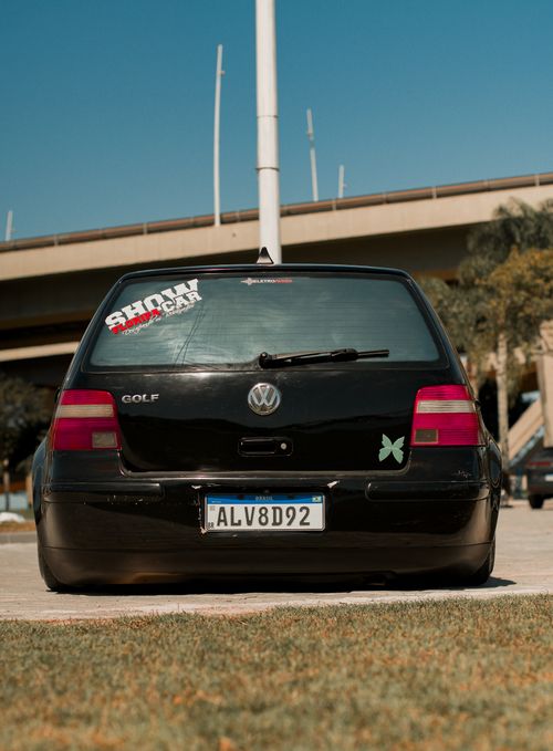 Free Black Volkswagen Golf with custom stickers, photographed from behind in a sunny urban setting. Stock Photo