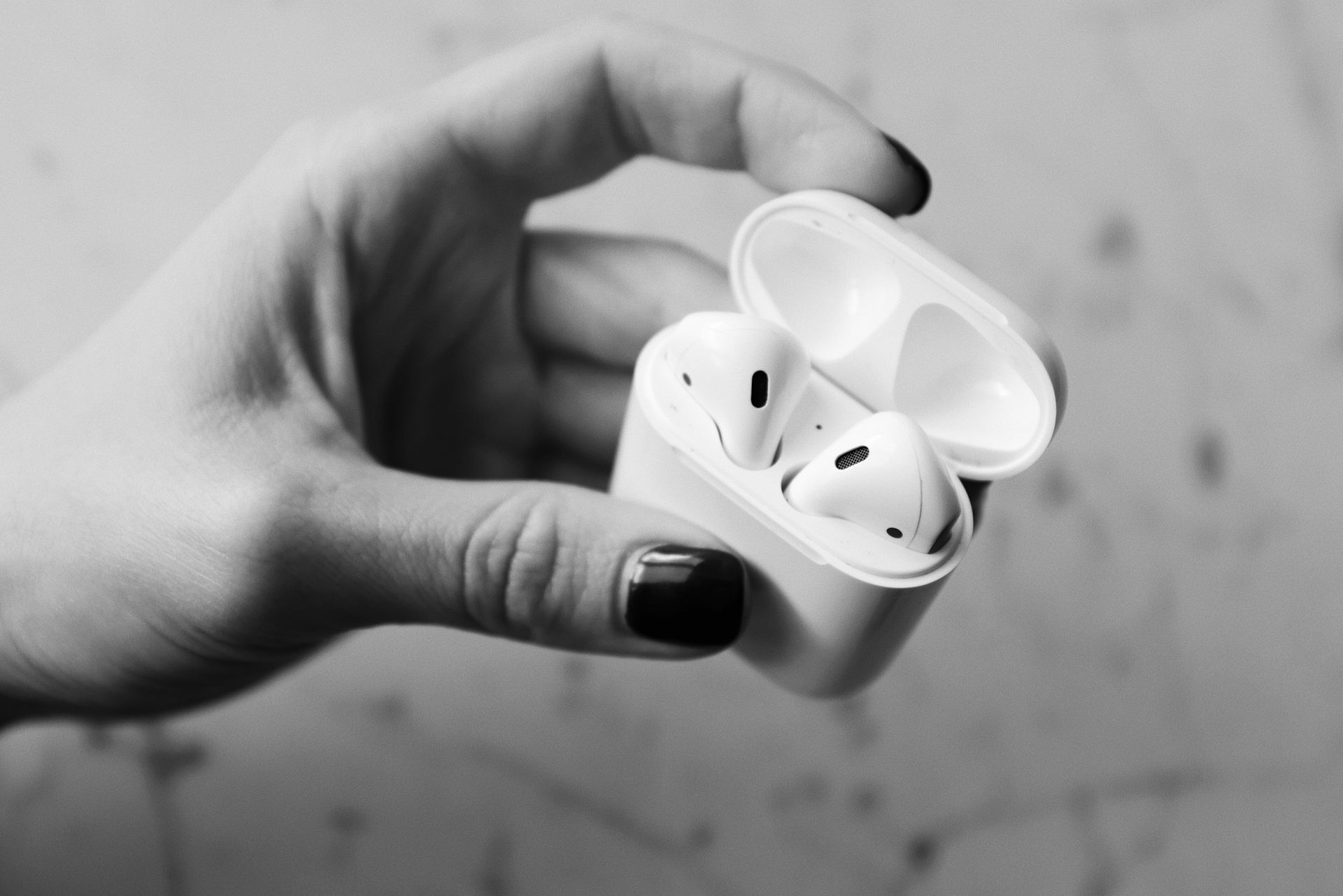 Black and white photo of a hand holding a case with wireless earbuds, showcasing portable technology.