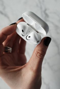 Detailed shot of wireless earbuds in hand against a marble background.